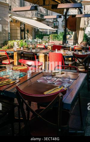 A charming European outdoor cafe with rustic wooden tables, vibrant red chairs, and decorative place settings, inviting travelers to relish a cozy din Stock Photo