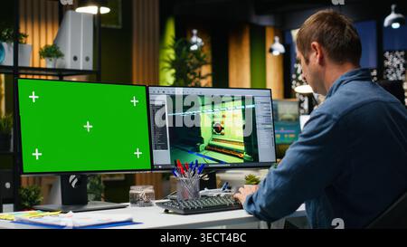 Chroma key with male employee working on game development, using dual monitors at workstation. Young expert engineer creating futuristic spaceship station on modern software. Camera B. Stock Photo