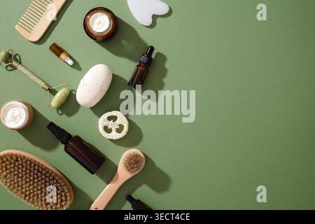 A top view of eco-friendly skincare items on a green background, featuring natural brushes, jade roller, glass dropper bottles, soap, and sustainable Stock Photo