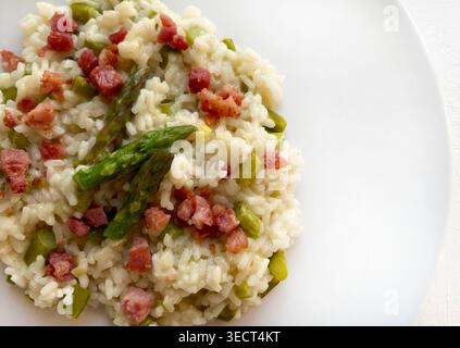 Close-up of a gourmet asparagus and crispy bacon risotto served on a modern plate. Bright, airy, and spring themed food photography. Overhead view. Stock Photo