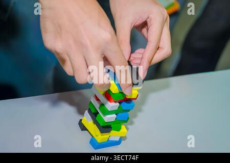 A person's hands balancing a colorful red blue green yellow wooden stacking tower block game on a table at an event inside the QSNCC in Bangkok. Stock Photo