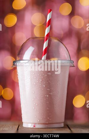 Strawberry milkshake in disposable plastic cup with striped straw and condensation droplets on wooden table Stock Photo