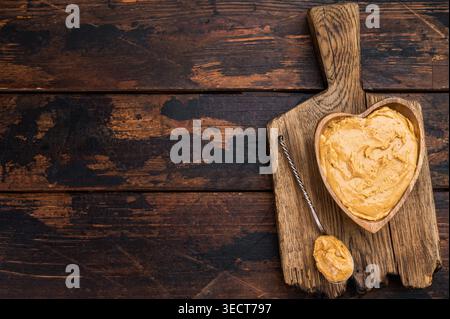 Creamy peanut butter spread in heart shaped wooden bowl on rustic cutting board with spoon. Natural peanut paste made from roasted peanuts Stock Photo