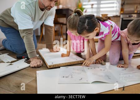 Engaged in a creative project, a father and his three daughters work together on a furniture assembly. Stock Photo