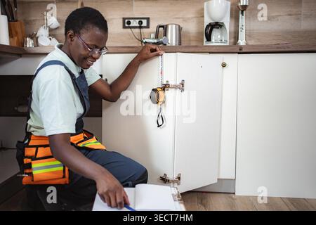 African american craftswoman working in kitchen using tape measure and taking notes Stock Photo