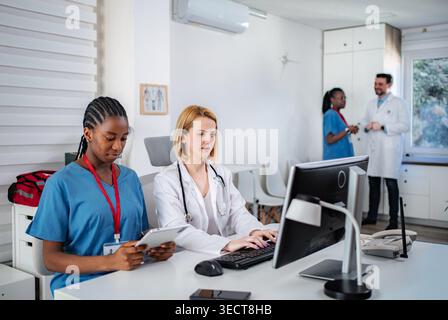 Healthcare team members collaborating in a clinic office, using computers and digital tablets Stock Photo