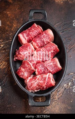 Fresh raw beef chunks for grilling or kebab, marbled meat in cast iron dish with herbs and spices, rustic cooking concept Stock Photo