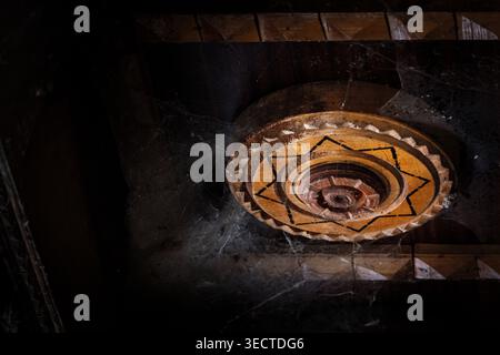 A single wooden rosette with a star motif rests within deep shadow coated in delicate cobwebs. The intricate hand carved design shows timeworn edges Stock Photo