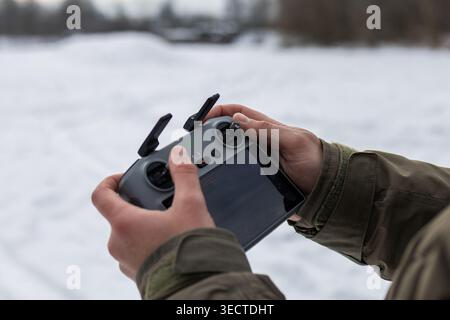 A pilot steadies a compact drone controller in cold air. Twin antennas rise while the display and joysticks prepare for flight during a focused winter Stock Photo