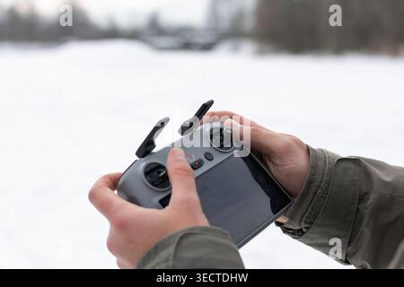 Gloved hands work a sturdy drone controller above snow. Buttons joysticks and a bright screen guide the aircraft as the operator readies for smooth Stock Photo
