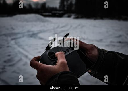 Moody evening tones surround a drone controller held against a dim winter field. Antennas and joysticks catch faint light as the pilot prepares for lo Stock Photo