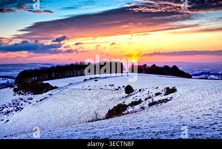 Winter sunset over Fontmell Down, Dorset UK paints snowy hills in pink and gold, capturing the quiet beauty of a freezing evening at dusk in winter. Stock Photo