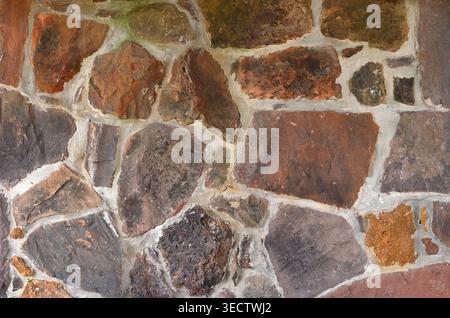 Multi stone and mortar wall surface closeup with red, gray, brown, and orange stones of various sizes and shapes, rough uneven surfaces, mortar crack, Stock Photo