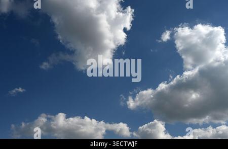 Partly clouded sky with large cloud formations, open blue sky between the clouds, dark to light blue gradient, and sunlight shining through Stock Photo