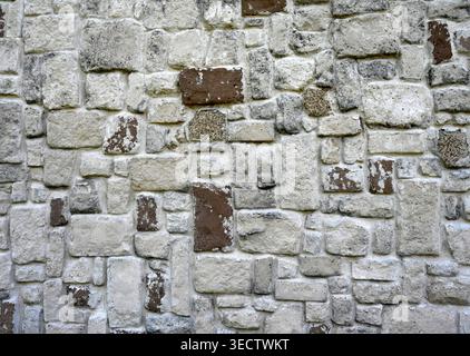 Rock wall with gray stones, painted brown stones, porous rough uneven surfaces, embedded pebbles, black smudges, and evenly troughed light gray mortar Stock Photo
