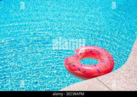 Pink donut shaped inflatable ring floating on clear blue swimming pool water. Bright summer vacation concept with copy space. Fun leisure, travel and Stock Photo