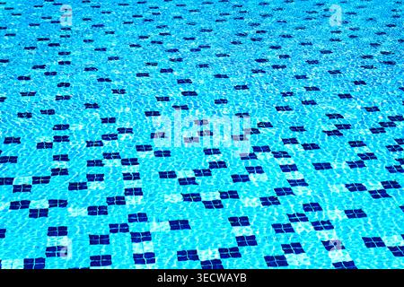 Clear blue swimming pool water with geometric tile pattern and sunlight reflections. Abstract background with copy space. Summer, refreshment and clea Stock Photo