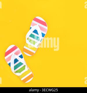Rainbow flip flops for holiday travel footwear on yellow background. Summer holiday casual fun fashionable rubber striped design. Stock Photo
