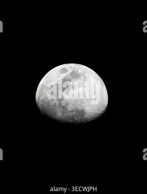 This image captures the Earth's Moon in a waxing gibbous phase, set against a stark, black background. The high-contrast lighting emphasizes the Moon' Stock Photo