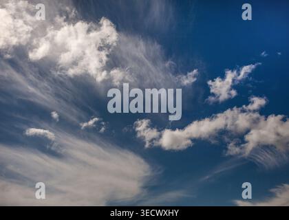 Wisps of cirrus drift across a deep blue sky while scattered cumulus clouds glow softly in the sunlight above. Stock Photo