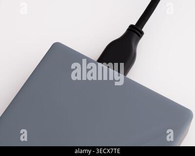 A close-up shot of a gray external hard drive with a black USB cable connected to it. White background. Stock Photo
