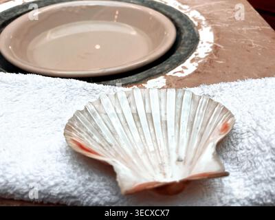 Clam shell used to scoop water out of a bowl of water in a font as part of the ritual of baptism in a catholic church Stock Photo