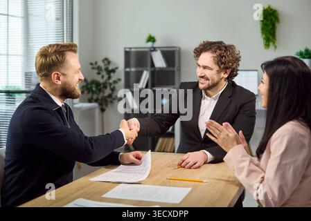 Recruiter and candidate shake hands after interview while colleague applauds Stock Photo
