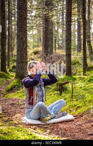 Woman practicing yoga meditation in peaceful forest Stock Photo