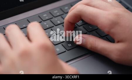 A young man typing on a modern laptop keyboard while studying, coding, or working on an IT project.  Close up. Stock Photo