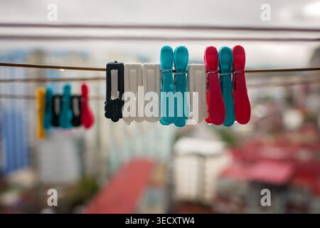 Bright multi-colored plastic clothespins with raindrops on a wire outdoors against a blurred city background. Concept of laundry and household. Stock Photo