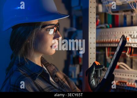 Female electrical engineer inspecting power system on tablet. Digital technical control. Stock Photo