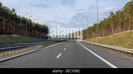 Empty highway leading through a forest. The motorway stretches into the distance. Stock Photo