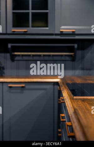 Corner kitchen with dark cabinets and wood. Modern countertop with built-in hob and decor. Stock Photo