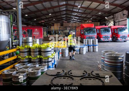 London, UK - 4 Jul 24: Warehouse scene at Fuller’s Griffin Brewery in Chiswick, London, with stacked beer kegs, a worker in high visibility vest, and Stock Photo