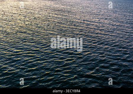 Sea surface during golden sunset light. Uniform texture of small ripples and waves. Stock Photo