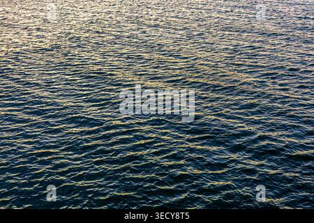 Ocean wave texture during beautiful sunset. Golden light illuminates the blue water surface. Stock Photo