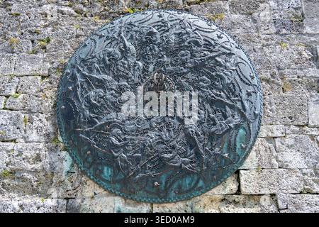 Gruyeres, Switzerland - 13 Jul 24: Detailed bronze round relief with dark patina mounted on a weathered stone wall at Château de Gruyères in Gruyères, Stock Photo