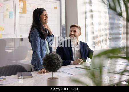 Two happy multiethnic male, female teammates laughing during joyful collaboration Stock Photo