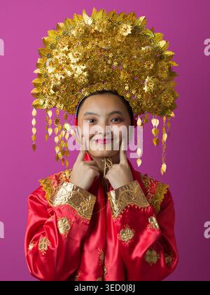 Portrait of Smiling Indonesian Asian Woman in Traditional Gold Headdress and Red Festive Costume for Celebration Stock Photo
