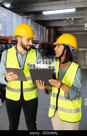 Two workers discussing logistics operations with tablet clipboard in warehouse Stock Photo
