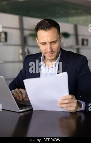 Businessman reviewing printed documents while working on laptop Stock Photo