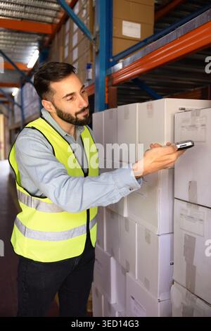 Worker scanning barcode on box stacked in industrial warehouse Stock Photo