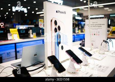Poznan, Poland - 26 July 2025: Modern electronics store displays iPhone 16 poster, multiple iPhones, MacBook laptop for sale. Stock Photo