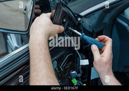 Focused assessment of mirror wiring and connectors. Technician meticulously examines mirror wiring harness and connectors using handheld tools and Stock Photo