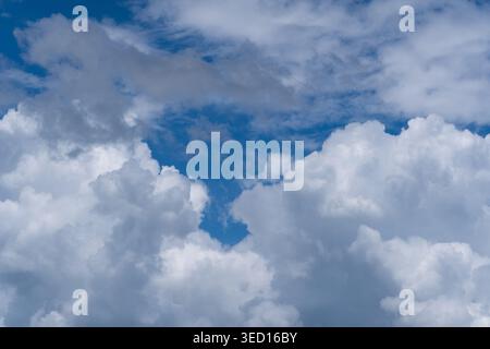 A high-resolution photograph of dramatic white cumulus clouds with deep gray shadows set against a vast, deep blue sky. The image captures the dynamic Stock Photo