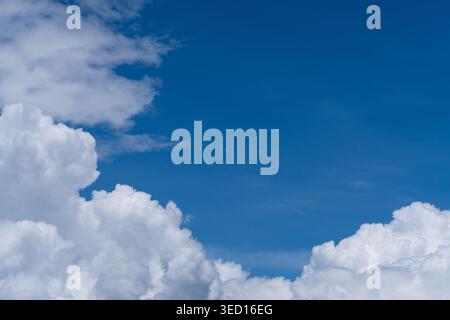 A high-angle natural shot of brilliant white puffy cumulus clouds gathered at the left and bottom of the frame, contrasting against a clear, vast deep Stock Photo