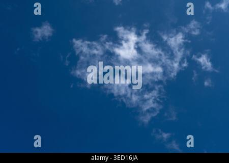 A minimalist nature photograph featuring a small, wispy white cloud floating in the center of a vast, clear deep blue sky. The high-contrast compositi Stock Photo