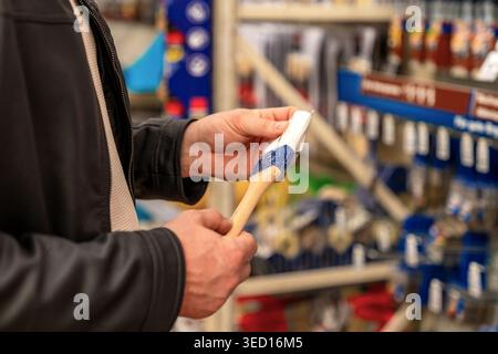 Caucasian professional painter prepares brush for job, hands loading bristles with paint, readying tool for application on renovation site, focused Stock Photo
