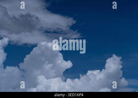 A high-contrast photograph capturing the layered texture of thick white cumulus clouds with grey undertones against a very deep, dark blue sky. The im Stock Photo