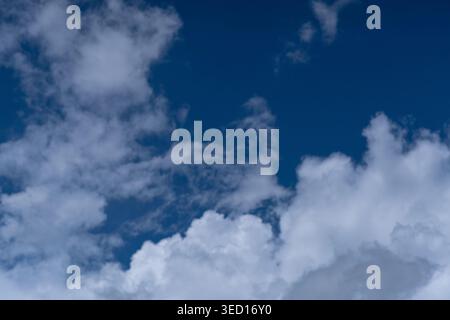 A photograph capturing a diagonal formation of scattered white cumulus clouds across a deep, dark blue sky. The image showcases the natural contrast a Stock Photo